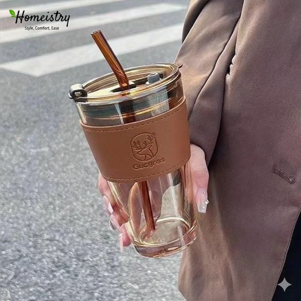 Clear glass tumbler with brown sleeve and straw held by a person on a street.