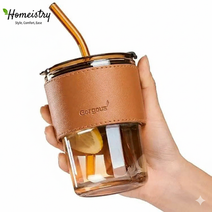 Hand holding a glass cup with a brown leather sleeve and straw, branded 'Gorgeous'.
